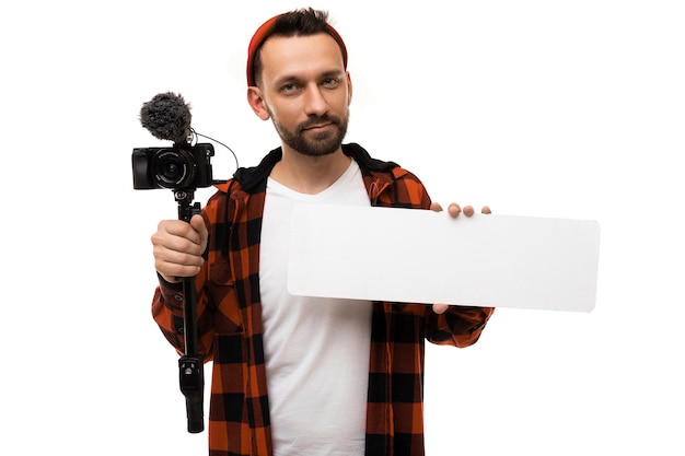 Un blogger uomo con una maglietta bianca e una maglietta in una gabbia rossa e nera con una videocamera e un