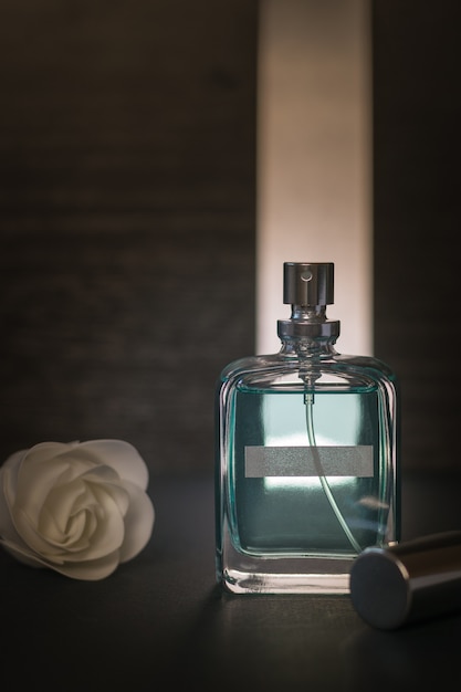 Un bocciolo di rosa bianco e una bottiglia di acqua profumata su uno sfondo nero in condizioni di luce intensa. Il concetto di cosmetici naturali.