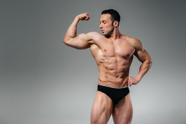 Un bodybuilder giovane atleta posa in studio in topless, mostrando i suoi addominali e muscoli. Sport.