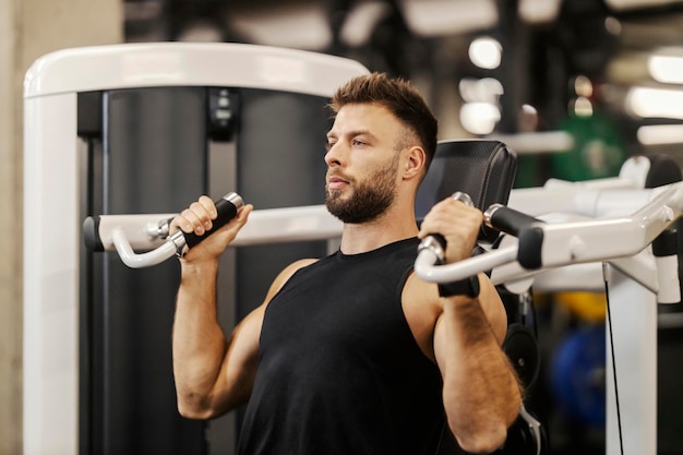 Un bodybuilder muscoloso in forma sta facendo esercizi su una macchina per la pressione del petto in una palestra