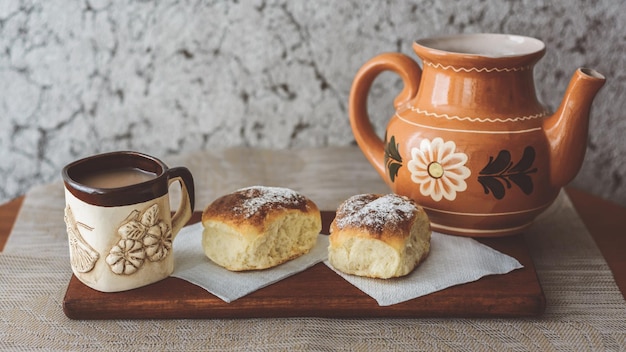 Un bollitore una tazza di caffè e due panini su una superficie di legno