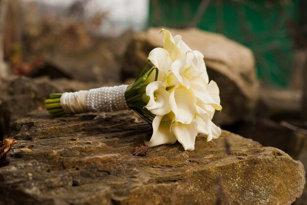 Un bouquet da sposa di gigli color crema giace su una pietra