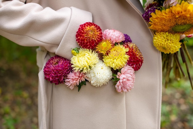 Un bouquet di fiori autunnali nella tasca di un cappotto beige