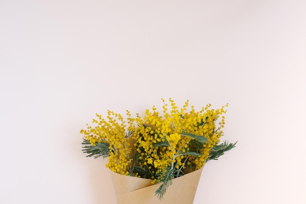 Un bouquet di fiori di mimosa in una borsa artigianale su uno sfondo bianco con uno spazio per le copie