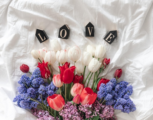 Un bouquet di fiori freschi e una parola decorativa amore in una vista dall'alto del letto bianco