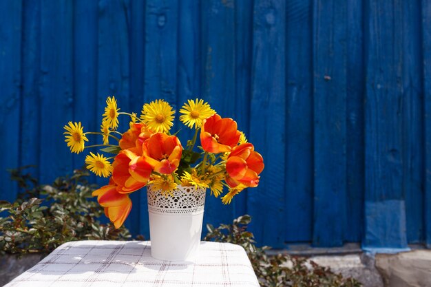 Un bouquet di fiori primaverili in un vaso bianco su uno sfondo di legno blu.