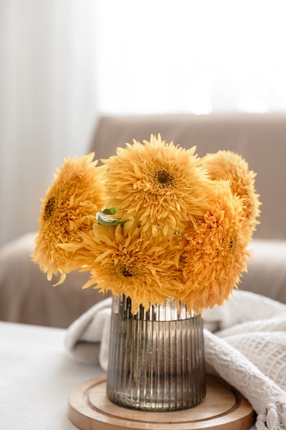 Un bouquet di girasoli luminosi in un vaso di vetro su uno sfondo sfocato all'interno della stanza.