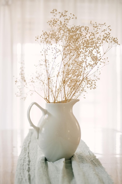 Un bouquet di gypsophila in una brocca bianca sullo sfondo della finestra