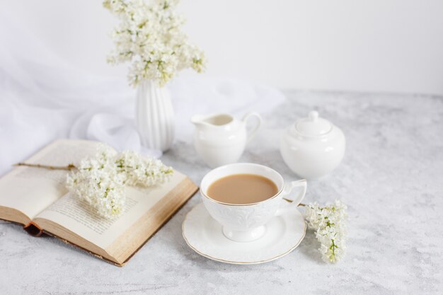 Un bouquet di lillà bianco, una tazza di caffè e un vecchio libro