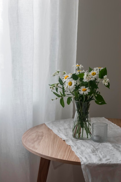 Un bouquet di margherite e gelsomino in un vaso di vetro su un tavolo rotondo in legno Concetto interno estivo