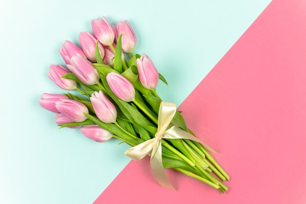 Un bouquet di tulipani rosa legati con un nastro su uno sfondo blu e rosa Fiori primaverili