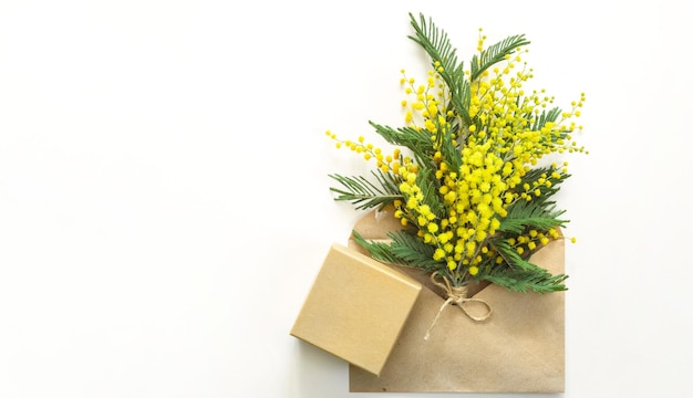 Un bouquet giallo di mimosa e una confezione regalo e un sacchetto di carta kraft Biglietto di auguri per il Festival di Primavera della Giornata Internazionale della Donna 8 marzo Pasqua Spazio di copia