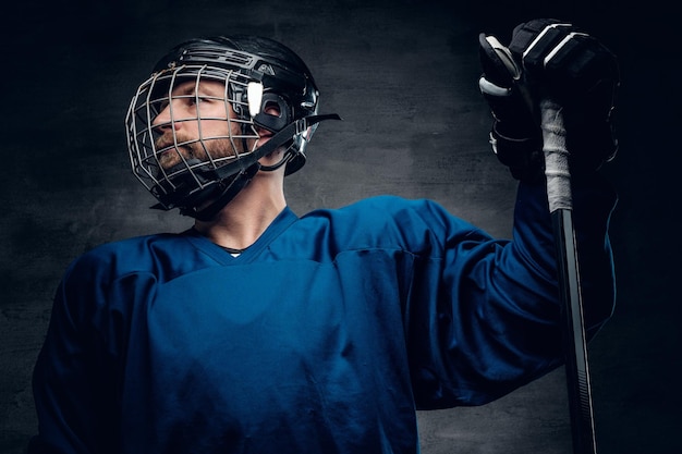 Un brutale giocatore di hockey su ghiaccio con la barba in casco di sicurezza tiene il bastone da gioco su uno sfondo grigio vignetta.