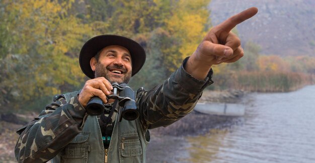 Un cacciatore con un cappello con un binocolo cerca la preda sullo sfondo della foresta