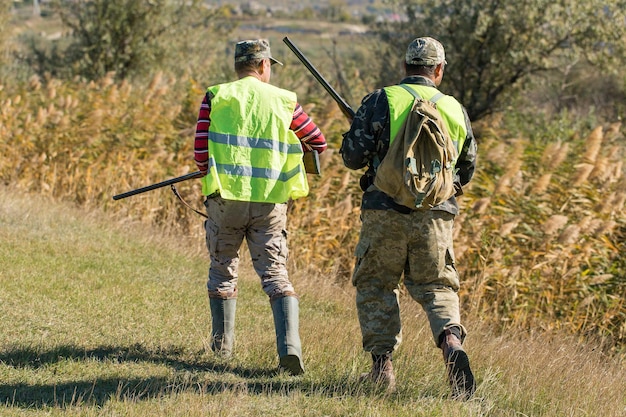 Un cacciatore con una pistola in mano in abiti da caccia nella foresta autunnale in cerca di un trofeo Un uomo in piedi con armi e cani da caccia che rintraccia la selvaggina
