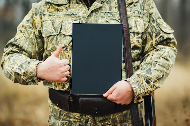 Un cacciatore con una pistola, tiene un'uniforme nera per la pubblicità sullo sfondo della foresta autunnale.