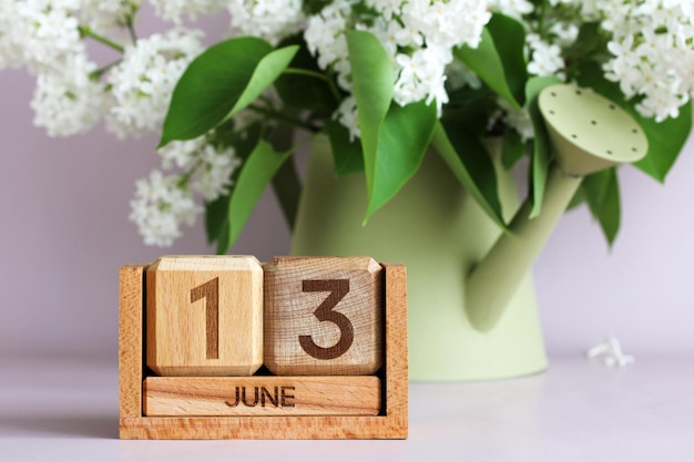 Un calendario di legno che mostra il 13 giugno e un lilac bianco in un'irrigazione decorativa possono indicare la data di un evento o di una celebrazione di compleanno