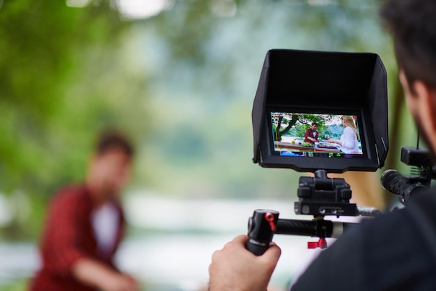 un cameraman professionalmente attrezzato sta filmando un gruppo di persone che cenano in riva al fiume.