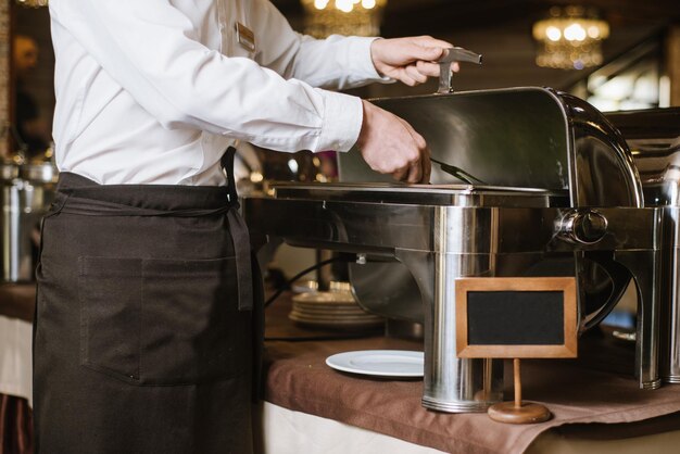 Un cameriere con le pinze prende una verdura dalla ciotola sul tavolo del buffet