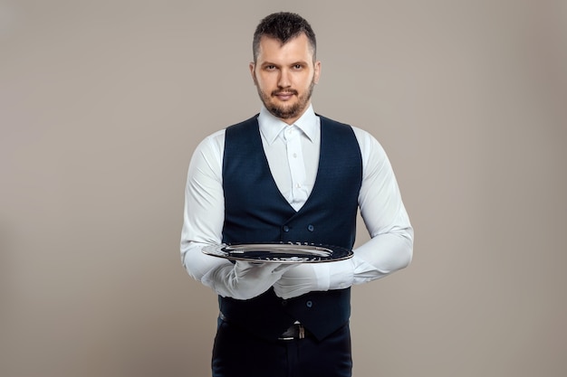 Un cameriere maschio con una camicia bianca e guanti bianchi sta con un vassoio d'argento. Il concetto di personale di servizio che serve i clienti in un ristorante.