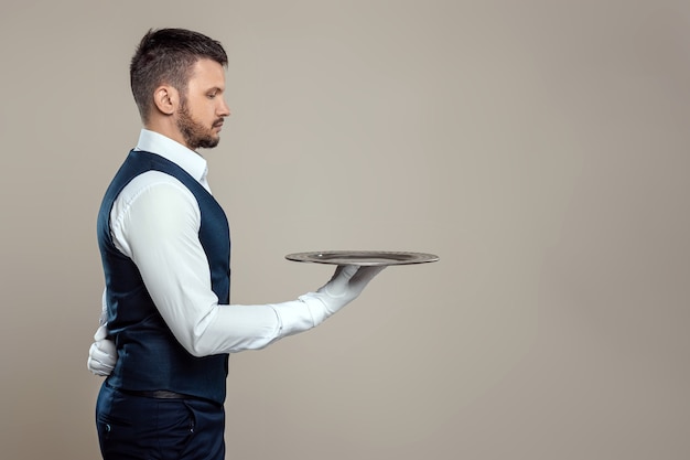 Un cameriere maschio con una camicia bianca è in piedi di lato con un vassoio d'argento. Il concetto di personale di servizio che serve i clienti in un ristorante.