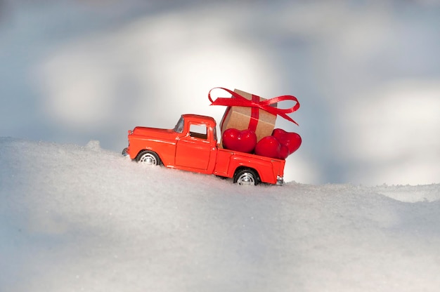 Un camioncino rosso trasporta cuori rossi e una confezione regalo con un fiocco rosso nella parte posteriore