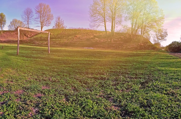 Un campo da calcio manuale verde con pali di legno e cancelli illuminati dal sole al tramonto