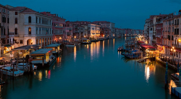 Un canale a Venezia di notte con luci sugli edifici e barche sull'acqua.