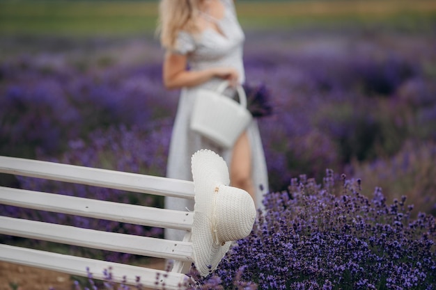 Un cappello bianco giace su una panchina sullo sfondo di una ragazza in un campo di lavanda vicino a Parigi