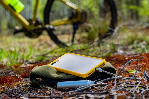 Un caricabatterie portatile carica lo smartphone Power Bank con cavo sullo sfondo della foresta e della bicicletta