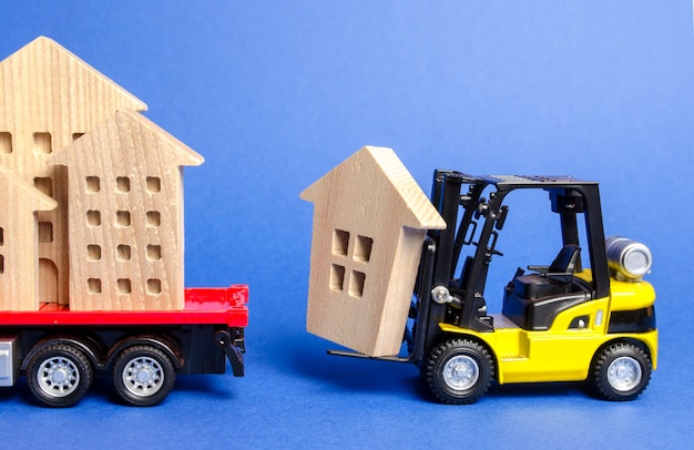 Un carrello elevatore giallo carica una figura di legno di una casa in un camion.