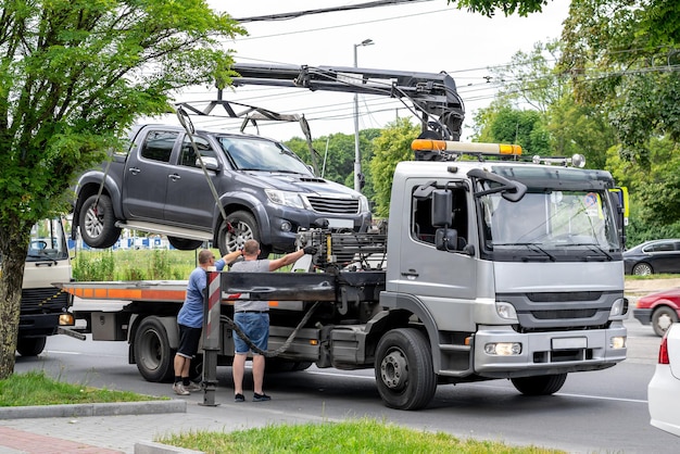 Un carro attrezzi grigio sulla carreggiata con un camioncino agganciato e due operatori