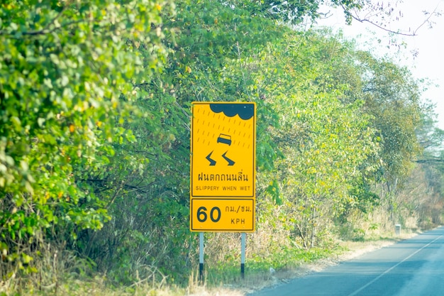 Un cartello che dice "Slippery when wet" e "60 KPH" è installato sul lato della strada.