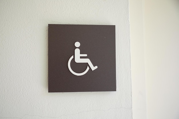 Un cartello per disabili è su un muro con sopra una sedia a rotelle.