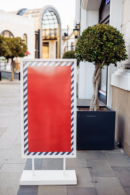 Un cartellone pubblicitario vuoto si trova sul marciapiede vicino agli alberi e all'architettura moderna durante il giorno