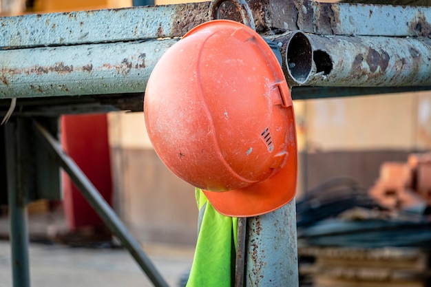 Un casco da lavoro arancione con un giubbotto di segnalazione è appeso all'impalcatura. Sfondo sfocato. Interruzione nei lavori di costruzione.