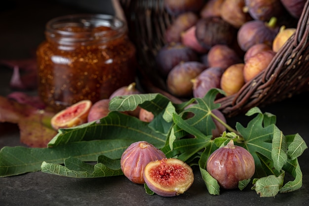 Un cesto di fichi freschi e un vasetto di marmellata di fichi su uno sfondo grigio scuro