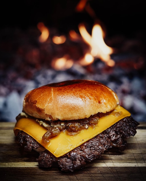 Un cheeseburger con cipolle e cipolle si trova su un tavolo di legno davanti a un fuoco.