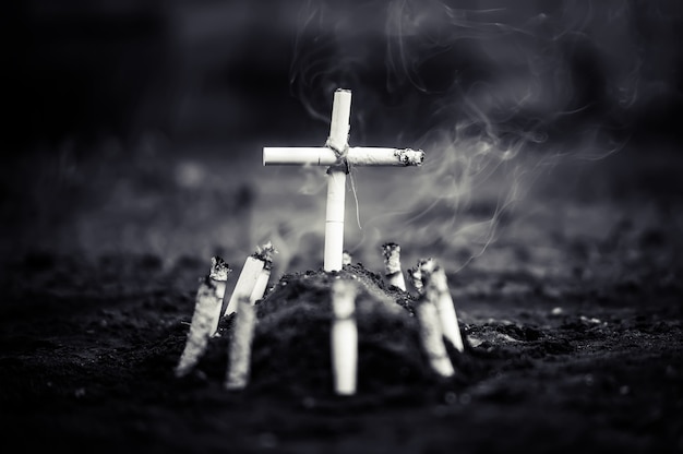 Un cimitero con una tomba fatta di sigarette. Morte per danno da nicotina o fumo di tabacco da sigarette. La sigaretta uccide. foto cupa in bianco e nero.