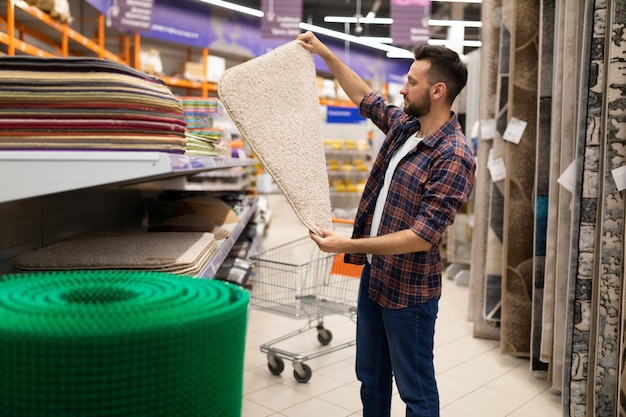 Un cliente maschio in un negozio di ferramenta sceglie un tappeto da bagno