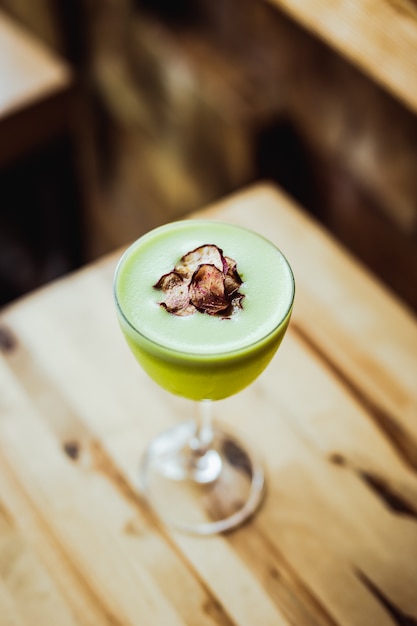 Un cocktail di tequila verde chiaro in un bicchiere nick and nora, contorno di chips di ravanello, su un tavolo di legno, angolo di 75 gradi