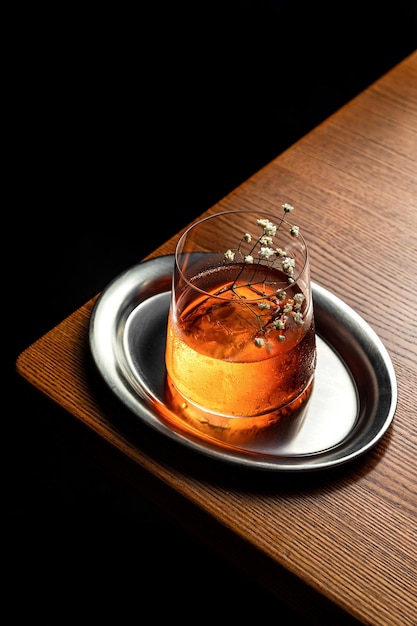 Un cocktail in un bicchiere Rock servito su un grande cubetto di ghiaccio e guarnito con fiori