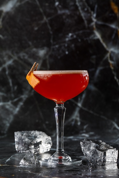 Un cocktail rosso acido in un bicchiere coupé guarnito con una buccia d'arancia Clover club con gin importato