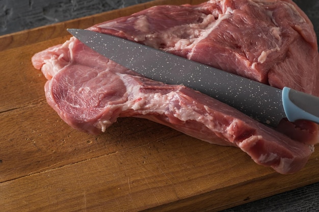 Un coltello taglia una bistecca di maiale da un grosso pezzo di carne su un tavolo di legno. Ingredienti per la cottura di piatti di carne.