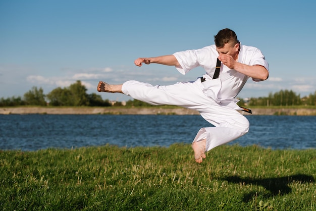 Un combattente di karate uomo in kimono bianco che si allena all'aperto nel parco