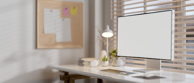 Un computer con un mockup dello schermo bianco su una scrivania contro la finestra in un moderno ufficio bianco