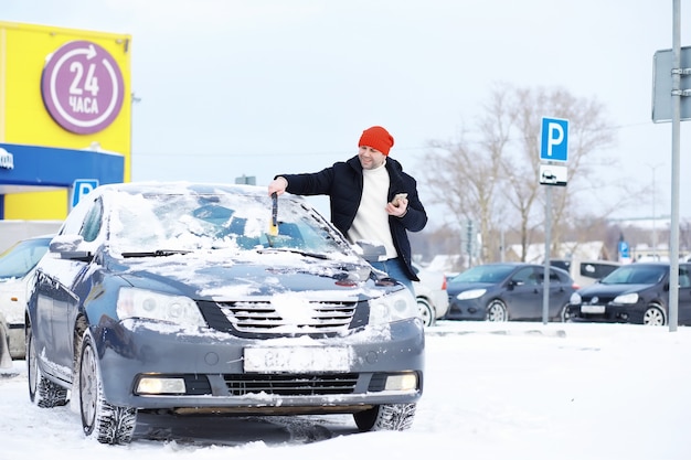 Un conducente di sesso maschile è in piedi davanti a un'auto. Il proprietario pulisce l'auto dalla neve in inverno. Auto dopo una nevicata.