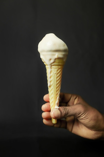 Un cono di gelato in mano su uno sfondo nero in primo piano