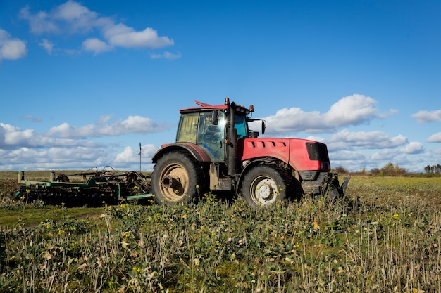 Un contadino in un trattore, macchine agricole, prepara la terra con un coltivatore. Un moderno trattore rosso in un campo. Arare un trattore pesante mentre si coltivano lavori agricoli in un campo con un aratro.