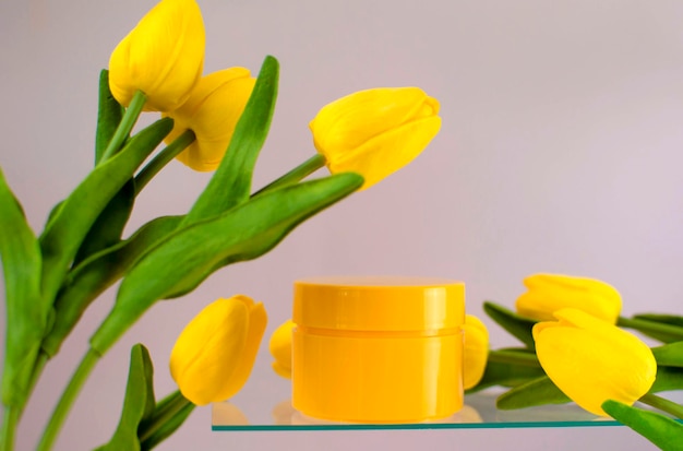 Un contenitore cosmetico giallo puro con un bouquet di tulipani su sfondo rosa. Imballaggio vuoto con etichette per il layout del marchio. Il concetto di cosmetici naturali primaverili, un banner di una vendita di cosmetici.